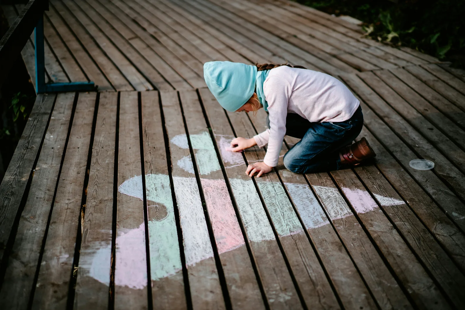 Child drawing hearts with chalk on a wooden boardwalk